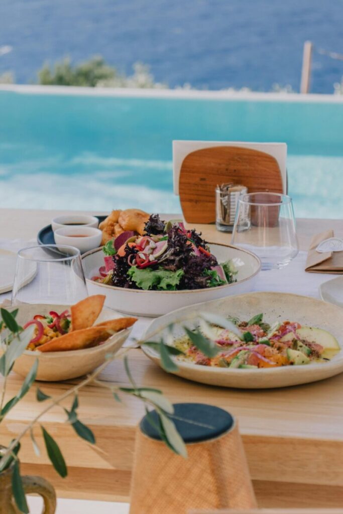 A lavish table setting with salads and plates by the pool overlooking the ocean.